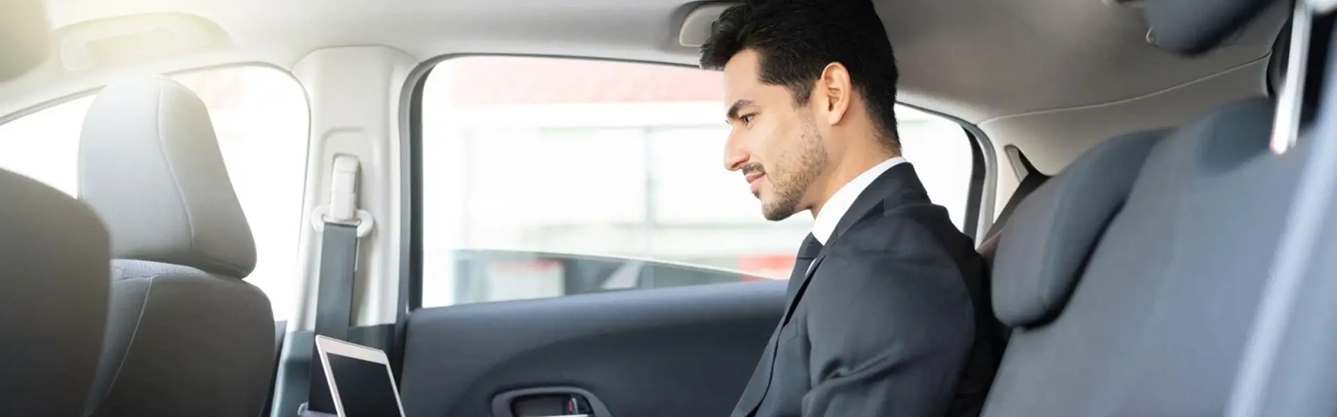 Business traveler sitting inside a comfortable vehicle using a tablet during a professional corporate transportation ride.